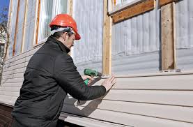 A man in an orange hard hat is using a drill to install siding.