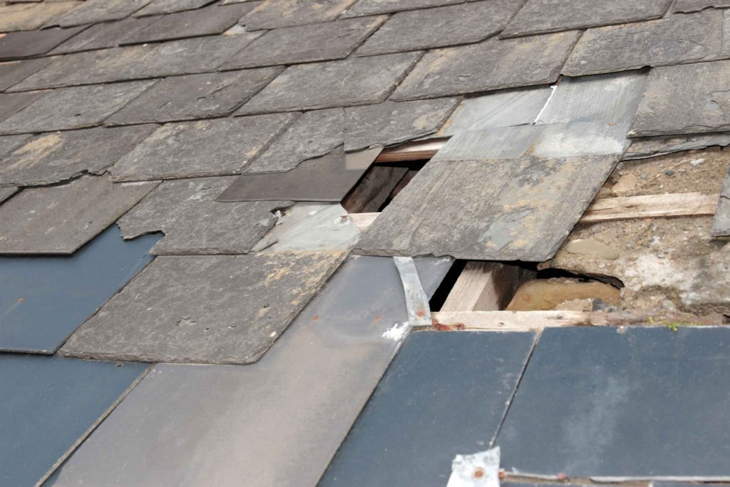 A broken roof with missing shingles and a hole in the middle.